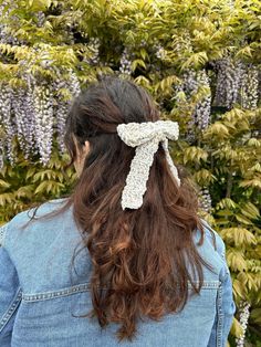 a woman with long hair wearing a white crochet bow in front of purple flowers