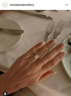 a woman's hand with a diamond ring on top of her finger next to a plate of food