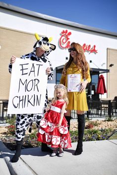 two women and a child are dressed up as cows, one is holding a sign that says eat more chicken