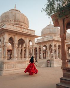 a woman in a red dress is walking through an old building with arches and pillars