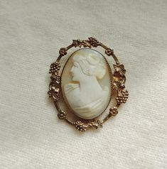 vintage cameo - carved shell cameo - gold filled cameo pin - vintage cameo brooch - authentic carved shell cameo pin - gold filled frame cameo brooch - shell cameo pin - lovely vintage piece - saw tooth bezel set hand carved oval shell brooch - pretty lady is looking left - pale cream bust fading to a delicate light pale pink - frame is set away from bezel - small gatherings of grapes and little five petaled forget me not flowers adorn the frame - twist locking pin closure on back - frame could Vintage Gold Carved Brooches, Antique White Cameo Brooch, Vintage Intaglio Brooches Gift, Vintage Carved Brooches For Gifts, Vintage Carved Brooches Gift, Vintage White Cameo Brooch, Vintage White Cameo Brooches, Forget Me Not Flowers, Rose Pale