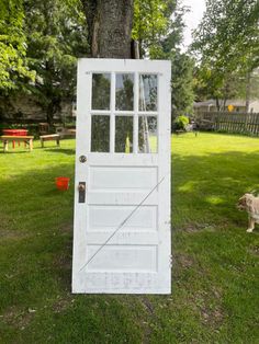 a white door sitting in the grass next to a tree and a dog walking by