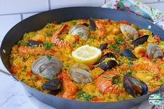 a pan filled with seafood and rice on top of a counter next to a lemon wedge