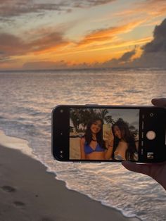 a person holding up a cell phone to take a photo on the beach at sunset