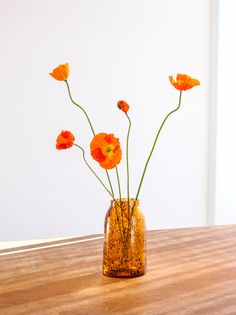 some orange flowers are in a vase on a wooden table with white walls behind them