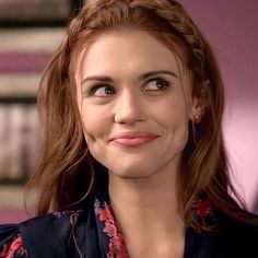 a close up of a person wearing a blouse and smiling at the camera with books in the background