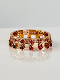 two gold rings with red stones are on a white surface and one is in the foreground