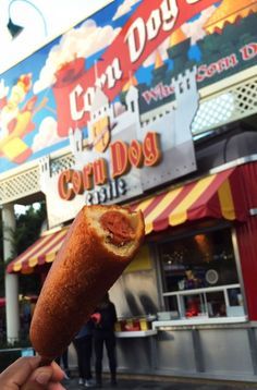 a person holding up a hot dog in front of a carnival ride sign and building