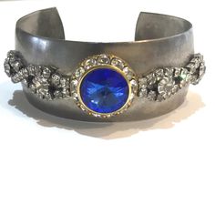 This listing is for a silver toned metal cuff bracelet adorned with vintage jewelry with a center blue rivoli rhinestone piece and clear rhinestone accents. Costume jewelry.  The bracelet is approximately 6 inches around the inside, 1 inch wide with a 1 and 2/8 inch opening. Non adjustable.  Please visit my shop for more unique jewelry with vintage accents. I combine shipping. First Class packages will be shipped bubble wrapped inside of a padded envelope. Priority Mail packages will be shipped bubble wrapped in a box. Any displays not included in sale unless otherwise noted. Coin in photo for size reference. Feel free to reach out with any questions, thank you for visiting my shop! Vintage Silver Jeweled Bracelets, Collectible Metal Jewelry With Jewels, Vintage Metal Jewelry With Bling, Vintage Silver Jeweled Jewelry, Vintage Jeweled Silver Jewelry, Silver Costume Jewelry Cuff Bangle, Silver Bangle Cuff Bracelet Costume Jewelry, Jeweled Metal Cuff Bracelet - Gift, Metal Jeweled Cuff Bracelet As Gift