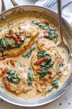 a pan filled with chicken and spinach on top of a white table next to silverware