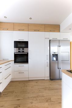 an empty kitchen with white cabinets and wood flooring on the countertops, along with a stainless steel refrigerator