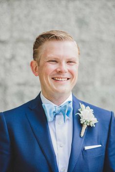 a man in a blue suit and bow tie smiles at the camera while wearing a boutonniere