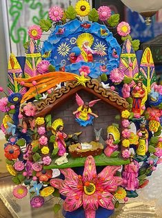 a colorful clock is on display in a store window with flowers and other decorations around it