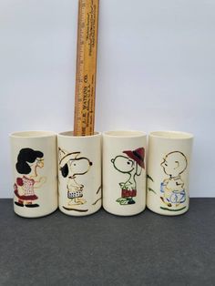 four cups with cartoon characters on them are next to a ruler