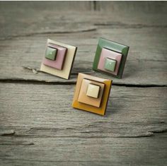 two square shaped earrings sitting on top of a wooden table