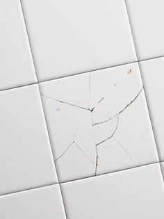 a white tiled wall with cracks in the middle and one broken piece on it's side