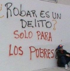 a man sitting on the ground next to a wall with graffiti written on it in spanish