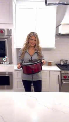 a woman standing in a kitchen holding a pot