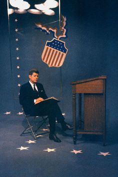 a man sitting in a chair with an american flag on the wall next to him