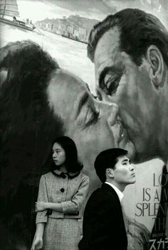 two people are standing in front of a large painting with a man and woman kissing