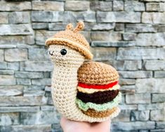 a hand holding a small crocheted stuffed animal with a hamburger on it's thumb