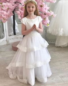 Buy jewel neck white first communion dress with layered skirts online at JJsprom.com Wedding Dress With Layered Tiered Skirt, Wedding Dress With Tiered Skirt And Layered Hem, Wedding Dress With Layered Hem And Tiered Skirt, White Layered Tiered Dress, White Tiered Layered Dress, White Layered Dress With Tiered Skirt, White Tiered Skirt Dress With Layered Details, White Princess Style Tiered Dress, Tiered Princess Dress For Wedding