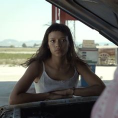 a woman sitting in the hood of a car with her hands on her hips and looking at the camera