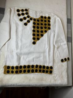 Ethiopian and Eritrean traditional men shirt pa long-sleeved white garment with decorative details. There is a prominent gold and black circular pattern across the upper chest area, as well as along the bottom hem and sleeve cuffs. The design on the chest appears to have an abstract triangular shape, extending towards the neck with circular motifs, giving it a unique and eye-catching look. Gold Long Sleeve Cotton Shirt, Traditional Long Sleeve Shirt With Patterns, Traditional White Shirt For Festivals, Traditional Long Sleeve Shirt, White Traditional Tops With Traditional Patterns, Traditional Long Sleeve Festive Shirt, Traditional Fit White Top, Traditional Fitted Long Sleeve Shirt, Fitted Long Sleeve Tops With Traditional Patterns