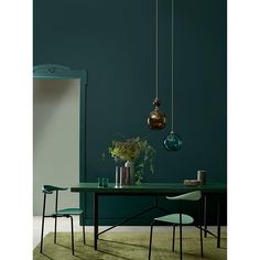 a dining table with green chairs and hanging lights in the corner, against a teal blue wall