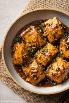 tofu with black beans in a bowl on top of a table next to chopsticks