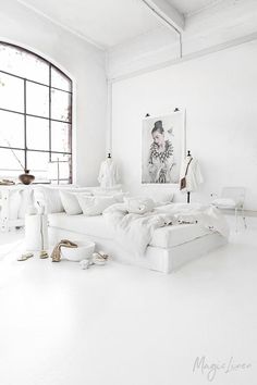 a white room with a large window and lots of pillows on the bed in front of it