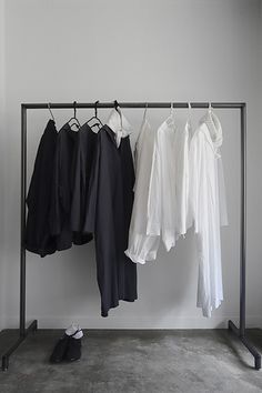 clothes are hanging on a rail in front of a white wall and black iron frame