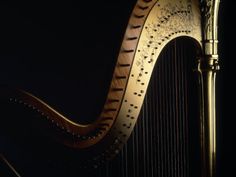 an ornate golden harp with strings in front of a black background and light from the side