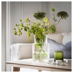 a glass vase filled with green flowers on top of a table next to two candles