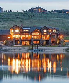 a large house sitting on top of a lush green hillside next to a lake at night