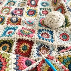 a crochet granny blanket with yarn and scissors on the ground next to it