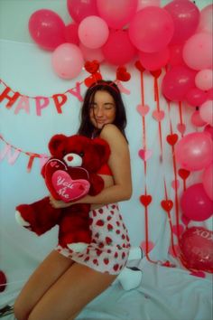 a woman holding a teddy bear in front of balloons