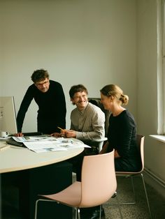 three people are sitting at a table working on a laptop