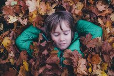 a young boy is laying in leaves with his head on his hands and eyes closed