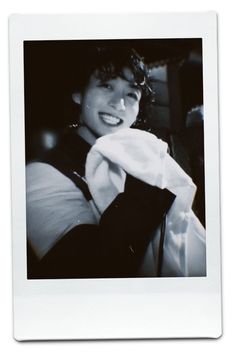 a black and white photo of a young man smiling with his hand on his tie