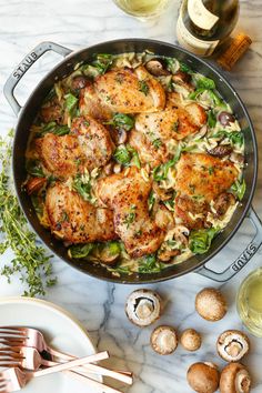 chicken and pasta with mushrooms in a skillet on a marble countertop next to wine glasses