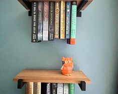 a cat figurine sitting on top of a wooden shelf next to several books