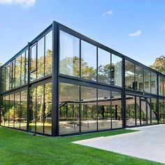 a large glass building sitting on top of a lush green field next to a forest