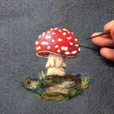 someone is needleing the top of a red mushroom with white dots on it's surface