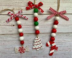 three christmas decorations hanging from strings on a white wooden surface with red, green and white ribbons