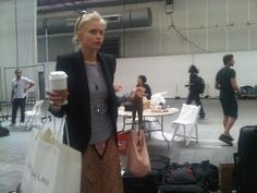 a woman is standing in an airport with her luggage and holding a coffee to go