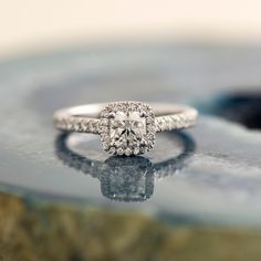 a diamond ring sitting on top of a marble slab with its reflection in the water