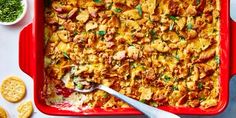 a red casserole dish filled with chicken, cheese and sauce next to crackers