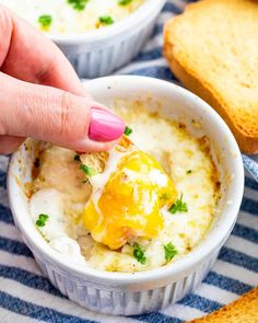 a hand dipping an egg into a bowl of mashed potatoes with bread in the background