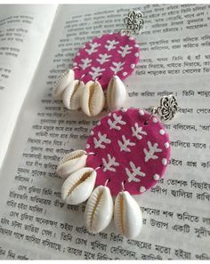 two seashells are attached to a pink and white fabric earring on top of an open book